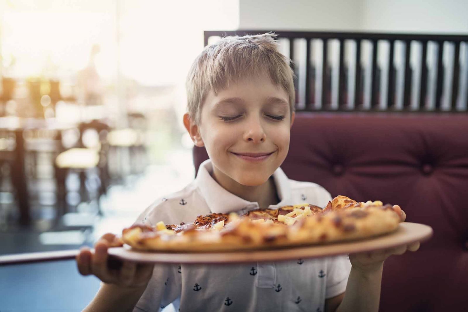 Boy holding a big pizza and smelling it