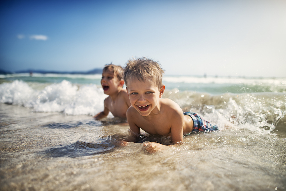 two little boys laying in the rolling waves on the beach